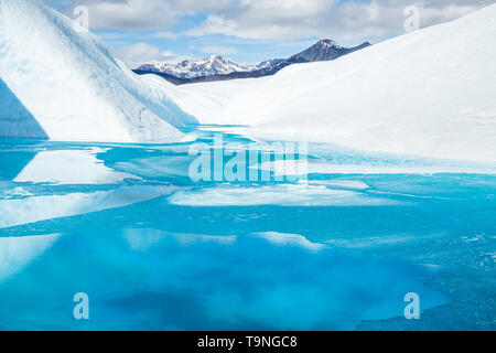 Ice on the surface of a partially frozen blue pool on the Matanuska Glacier of the Alaskan Chugach Mountains. Stock Photo