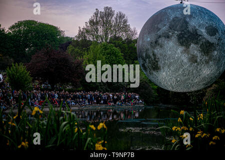 May 18, 2019 - Artist Luke Jerram's 7 metre diameter inflatable moon is suspended over the pond at Queens Park in Brighton during the Brighton Festival. The illuminated lunar model is one of several copies that tour the world for Luke's temporary exhibition. It features detailed NASA images of the moon's surface, with every centimetre of the lit sphere representing 5km of the moon's surface. The free arts event is part of the Brighton Festival, which is an annual celebration of art, music, theatre, dance, circus, and literature, which takes place in the city of Brighton and Hove during the m