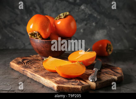 Ripe persimmons in bowl and on wooden board Stock Photo