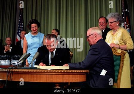 President Lyndon B. Johnson signing the Medicare Bill at the Harry S. Truman Library in Independence, Missouri. Former president Harry S. Truman is seated at the table with President Johnson. The following are in the background (from left to right): Senator Edward V. Long, an unidentified man, Lady Bird Johnson, Senator Mike Mansfield, Vice President Hubert Humphrey, and Bess Truman. July 30, 1965 Stock Photo