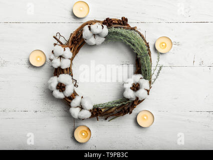 Wreath with cotton flowers and candles on white wooden background Stock Photo