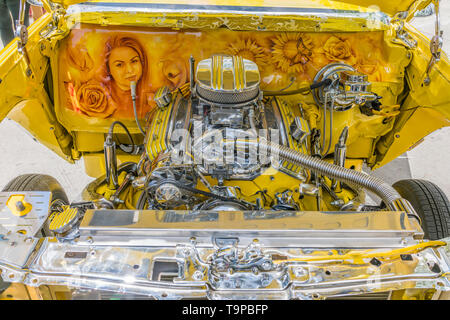 A view of the chromed and painted engine compartment, including hand painted woman's portrait and flowers, on a bright yellow Chevrolet lowrider car t Stock Photo