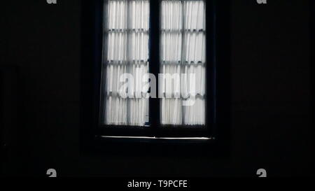 White sheer curtains over casement windows, dark inside, bright light outside.  A metaphor for isolation, agoraphobia or privacy. Stock Photo