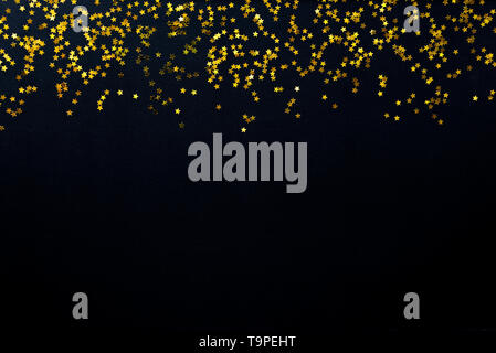 Star shaped golden sequins on a black background. Stock Photo