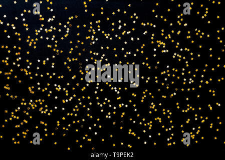 Star shaped golden sequins on a black background. Stock Photo