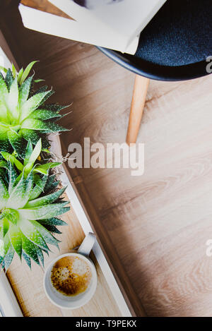 Top view of  books and magazines left on a chair, cup of coffee and succulent plants by the window. Concept of recreational time and space. Stock Photo