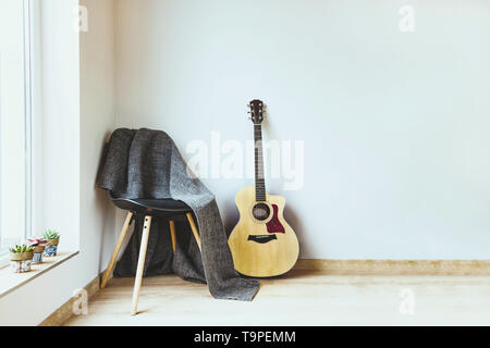 Contemporary home interior. Black chair covered with woolen gray blanket and acoustic guitar in front of an empty white wall. Succulent plants on the  Stock Photo