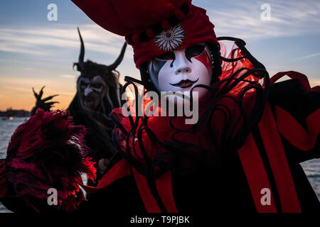 Portrait of a feminin masked person in a beautiful creative harlequin costume, posing at Grand Canal, Canal Grande, celebrating the Venetian Carnival Stock Photo