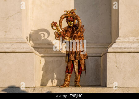 A masculin masked person in a beautiful creative harlequin costume, posing on the island San Giorgio di Maggiore, celebrating the Venetian Carnival Stock Photo