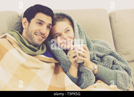 Young couple relaxing together, lying on sofa under blanket watching TV Stock Photo
