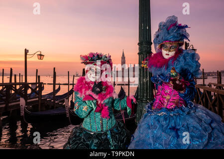 Portraits of a masked couple in beautiful creative costumes, posing at Grand Canal, Canal Grande, celebrating the Venetian Carnival Stock Photo