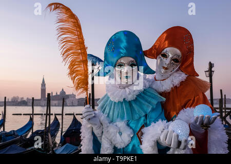 Portraits of a masked couple in beautiful creative costumes, posing at Grand Canal, Canal Grande, celebrating the Venetian Carnival Stock Photo