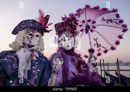 Portraits of a masked couple in beautiful creative costumes, posing at Grand Canal, Canal Grande, celebrating the Venetian Carnival Stock Photo