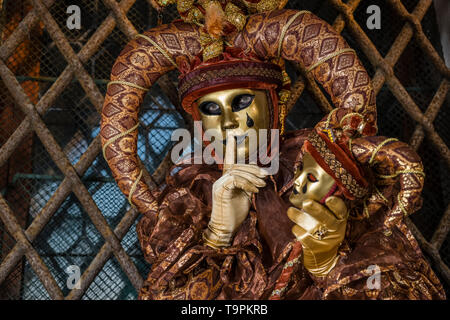 Portrait of a masculin masked person in a beautiful creative harlequin costume, posing in the arcades of the Doge's Palace, Palazzo Ducale Stock Photo