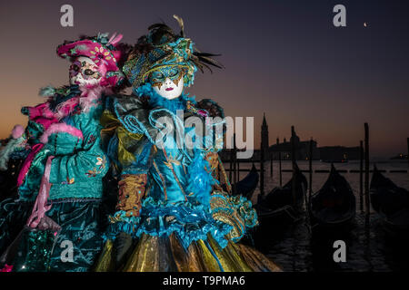 Portraits of a masked couple in beautiful creative costumes, posing at Grand Canal, Canal Grande, celebrating the Venetian Carnival Stock Photo