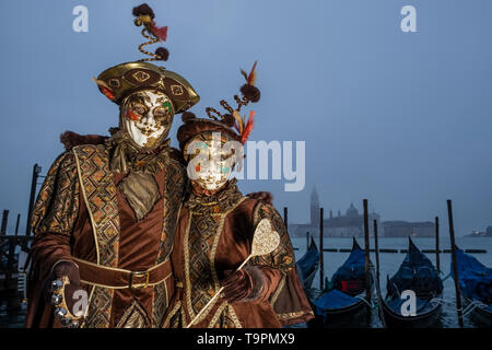 Portraits of a masked couple in beautiful creative costumes, posing at Grand Canal, Canal Grande, celebrating the Venetian Carnival Stock Photo