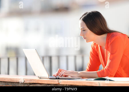 Side view portrait of a self employed writing on laptop in a balcony Stock Photo