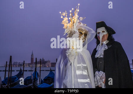 Portraits of a masked couple in beautiful creative costumes, posing at Grand Canal, Canal Grande, celebrating the Venetian Carnival Stock Photo