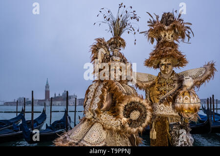 Portraits of a masked couple in beautiful creative costumes, posing at Grand Canal, Canal Grande, celebrating the Venetian Carnival Stock Photo