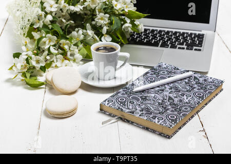 Work space with a laptop, a cup of tea and flowers on the wooden background. Home office composition, freelance concept Stock Photo
