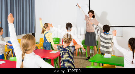 Young friendly female teacher conducting little warm-up with pupils during  break in lesson in elementary school Stock Photo