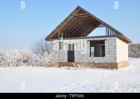 Building a Home During Winter. Building new house from autoclaved aerated concrete blocks vs bricks with unfinished roofing metal tiles construction. Stock Photo