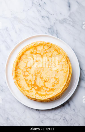 Crepes, thin pancakes on a white plate. Marble background. Copy cpace. Top view. Stock Photo