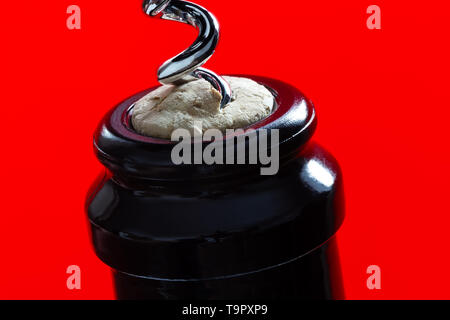 The neck of a dark bottle with a cork and a corkscrew on a red background Stock Photo
