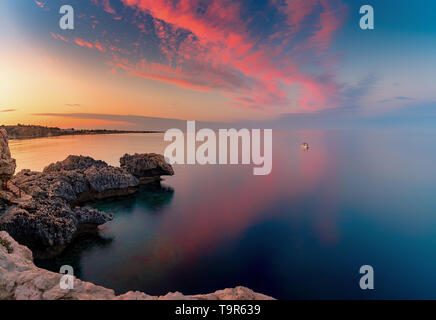 Amazing sunset image of Cape Greco cliffs and rocks on a sunset in Paralimni, Cyprus. Colorful red, pink and yellow skies with turquoise blue sea. Stock Photo