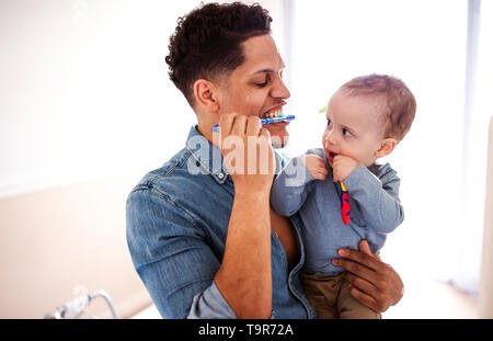 Father and small toddler son in a bathroom indoors at home, brushing teeth. Stock Photo