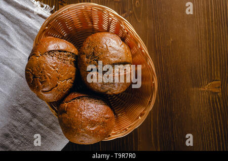 Craft three bread buns in a wicker basket, on a wooden cutting board. Simple breakfast on wooden background. Close-up view. copy space Stock Photo