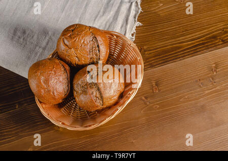 Craft three bread buns in a wicker basket, on a wooden cutting board. Simple breakfast on wooden background. Close-up view. copy space Stock Photo