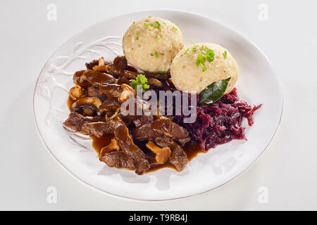 Plate of tasty Swiss ragout with strips of meat in a rich gravy with mushrooms served with red cabbage and dumplings garnished with herbs Stock Photo