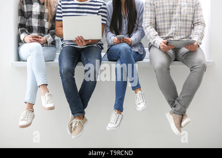 Young people with modern devices sitting on windowsill indoors Stock Photo