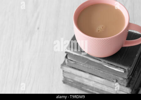 Cup of tea in a pink cup on a stack of old antique books with selective colour on a grey wood background Stock Photo