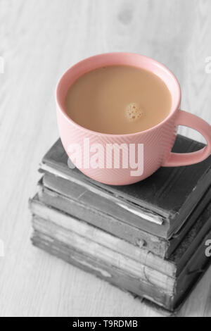Cup of tea in a pink cup on a stack of old antique books with selective colour on a grey wood background Stock Photo
