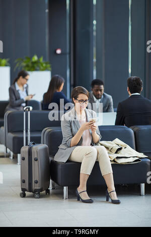 Happy woman sending message on phone in airport Stock Photo