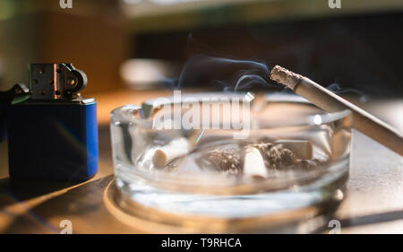 Cigarette burning in ash trail with blue metal lighter next to Stock Photo