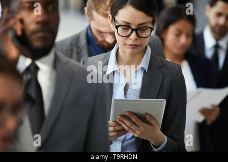 Busy lady reading document on tablet while standing in line Stock Photo
