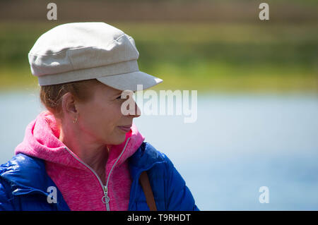 Caucasian middle aged woman wearing a baker boy hat looking out across water Stock Photo
