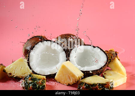 Cut ripe coconuts and pineapple with splash of water on color background Stock Photo
