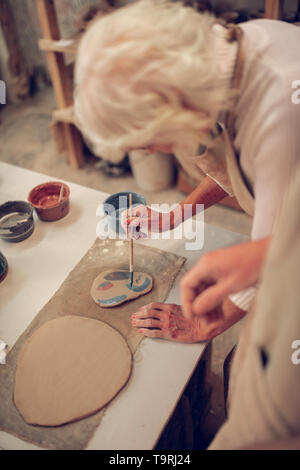 Nice grey haired woman looking at her painting Stock Photo