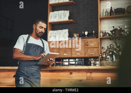 Young man in apron using digital tablet at his cafe Stock Photo