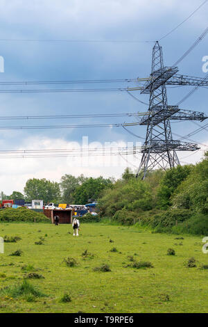 View across a field of a large electricity pylon, power lines and car scrapyard in Nursling, Test Valley, Southampton, Hampshire, southern England, UK