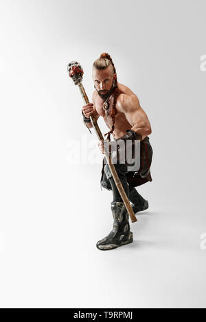 Serious long hair and muscular male model in leather viking's costume with the big mace cosplaying isolated on white studio background. Full-length portrait. Fantasy warrior, antique battle concept. Stock Photo