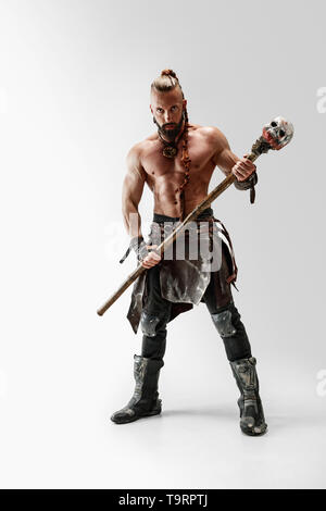 Serious long hair and muscular male model in leather viking's costume with the big mace cosplaying isolated on white studio background. Full-length portrait. Fantasy warrior, antique battle concept. Stock Photo