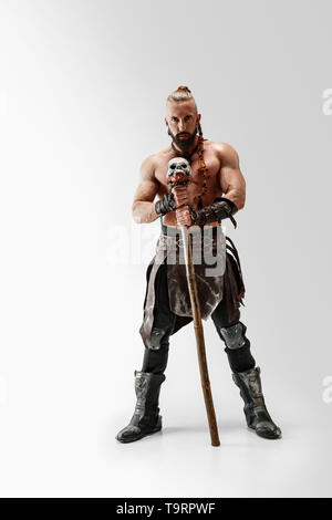 Serious long hair and muscular male model in leather viking's costume with the big mace cosplaying isolated on white studio background. Full-length portrait. Fantasy warrior, antique battle concept. Stock Photo