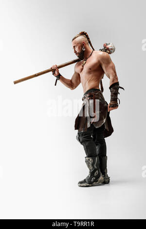 Serious long hair and muscular male model in leather viking's costume with the big mace cosplaying isolated on white studio background. Full-length portrait. Fantasy warrior, antique battle concept. Stock Photo