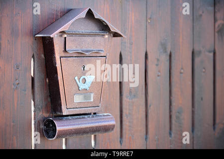 Brown textured metal postbox with a mail horn icon hanging on a wooden fence. Concept of mailbox and post delivery with copy space. Stock Photo