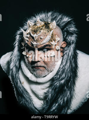 Severe emperor of perpetual cold realm wearing white fur coat with hood. Demon with horns on head and golden shining skin isolated on black background Stock Photo